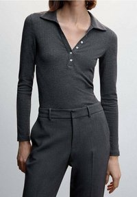 Grijze polo met lange mouwen en een gestructureerd patroon, knoopsluiting en een kraag. Gecombineerd met grijze op maat gemaakte broek.