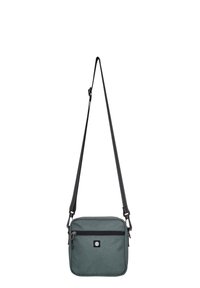 Zelená látková crossbody taška s texturovaným povrchem, černým zipem, černým popruhem a logo nášivkou na přední straně. Čtvercový tvar a lehký design.