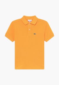 Pomarańczowa koszulka polo wykonana z bawełny; ma klasyczny kołnierzyk, zapięcie na trzy guziki oraz zielone logo krokodyla po lewej stronie klatki piersiowej.