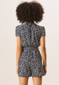 Navy blue romper with short sleeves, featuring a white abstract pattern, cinched waist, and a relaxed fit with shorts. Back view shown.
