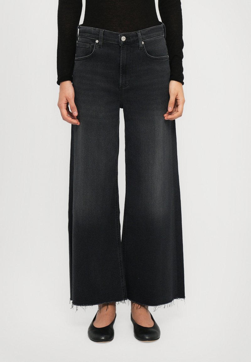 Jean en denim noir à jambes larges avec un ourlet effiloché, présentant un design classique à cinq poches et des accessoires en métal argenté au niveau de la taille.