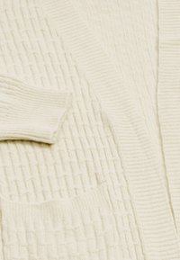 Cardigan a maglia color crema con polsini texturizzati a coste e colletto con apertura frontale.