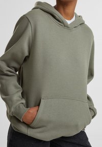 Sweat à capuche vert en matière douce, doté d'une poche kangourou et de poignets côtelés, avec une coupe décontractée et un design minimaliste.