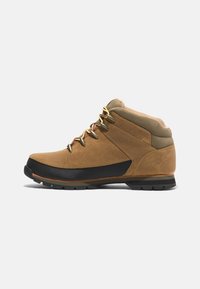 Braune Wanderschuhe aus Leder mit einer schwarzen Gummikappe, beigemTextilkragen und goldenen Ösen, ausgestattet mit einer robusten Sohle für besseren Halt.