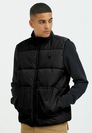 Zwarte puffer vest met een hoge kraag, ritssluiting aan de voorkant en een gestikt patroon. Voorzien van twee zakken aan de voorkant en een logo detail op de borst.