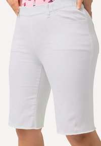 Bermuda shorts in denim bianco con vita aderente, tasche frontali e orlo risvoltato, che illustrano un tessuto liscio e texturizzato.