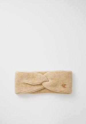 Knit headband in light beige, featuring a twisted design at the front and subtle ribbing. Small gold logo accent on the side.