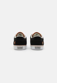 Black suede sneakers with white rubber soles, orange accents on the collar, and Etnies logo on the heel. Classic low-top design.
