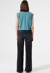 Türkises Kurzarmoberteil mit umgeschlagenen Schultern, kombiniert mit weiten schwarzen Jeans. Der Stoff sieht weich aus und hat eine lockere Passform mit minimalen Nähten.