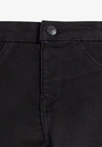 Jeans de mezclilla negra con un diseño clásico de cinco bolsillos, cierre de botón en la cintura y sutilezas en los detalles de costura.