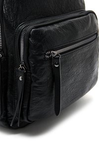 Zaino in pelle nera con superficie texture, dotato di molteplici tasche con zip e un design resistente. Accenti in hardware riflettente argentato.