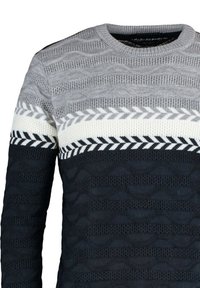 Pull en tricot gris avec un motif en vague texturé, orné de rayures alternées de motifs géométriques blancs et noirs le long de l'ourlet.