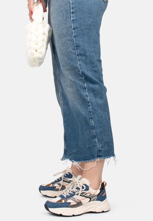 Les baskets présentent un mélange de matériaux avec un schéma de couleurs bleu et crème, une tige texturée et une semelle épaisse. Le bas des jeans est effiloché.