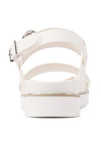 Sandal bianca con tomaia in sintetico liscia, cinturino alla caviglia regolabile e tacco basso a zeppa con un accento metallico lungo la suola.