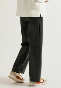 Schwarze Kunstlederhosen mit geradem Schnitt und glatter Textur. Kombiniert mit beigen und orangefarbenen Sneakern.