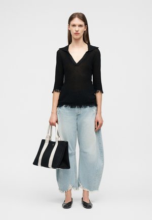 Naine, kes kannab musta V-kaelusega toppi, helesiniseid laia säärega rebenenud teksaseid, musti madalaid jalanõusid ja hoiab käes musta rahakotti valgete rihmadega.