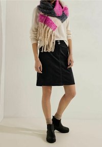 Sort denim-nederdel med to frontknapper, parret med en lys sweater, et flerfarvet frynse-halstørklæde og sorte ankelstøvler.
