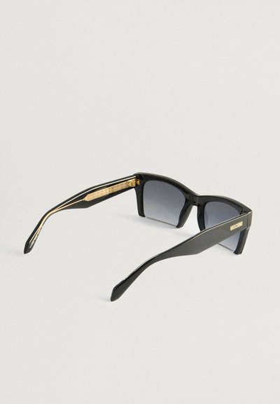 Óculos de sol pretos com lentes escuras, design angular e acabamentos texturizados em dourado nas hastes. Nome da marca "Moschino" exibido em uma das hastes.