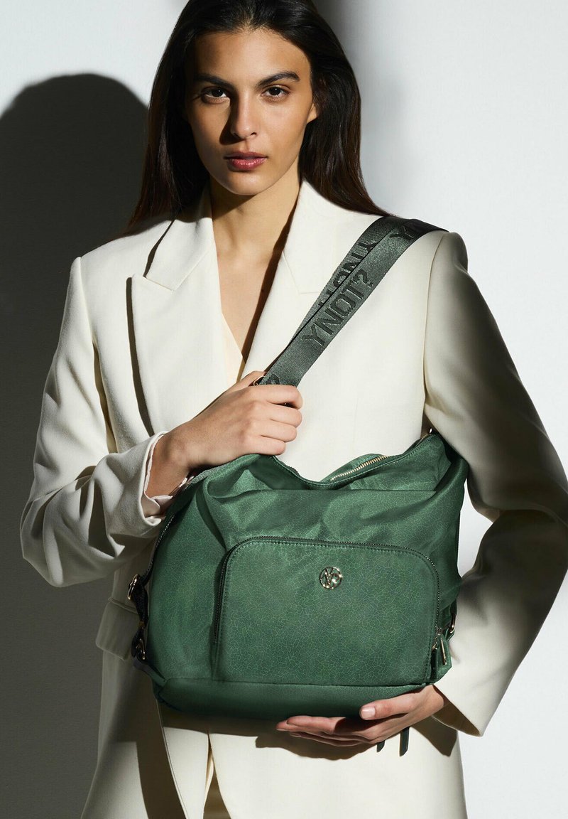 Borsa a tracolla verde con texture, dotata di un comparto principale con zip e tasca frontale. Presenta una tracolla larga con testo stampato. Superficie liscia, senza motivi.