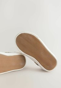 Weiße Sneaker mit einer Gummisohle; glattes Gummimaterial oben und strukturiertes Fischgrätmuster auf der Sohle. Sauberes Design, minimale Akzente.