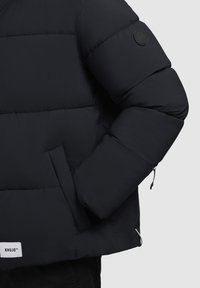 Must must jacket, millekeska, elastne mansett, külgtasku ja ümmargune logo märgis varrukal.