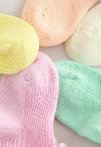 Seis gorritos de bebé tejidos en colores pastel: amarillo, melocotón, crema, rosa y verde menta, dispuestos juntos.