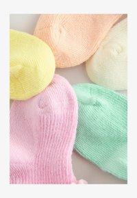 Seis gorritos de bebé tejidos en colores pastel: amarillo, melocotón, crema, rosa y verde menta, dispuestos juntos.