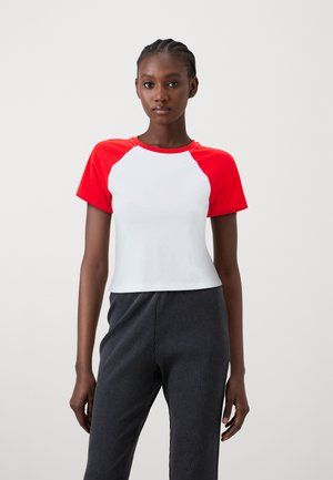 Valkoinen lyhythihainen t-paita, jossa on punaiset raglan-hihat. Pehmeä kangas, pyöreä kaulus, puristava muotoilu. Yhdistetty tummiin ribbiponteihin, sileä tekstuuri.