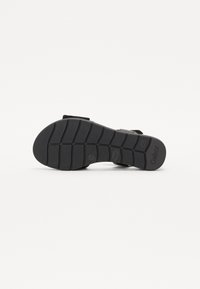 Black sandal sole with textured grip patterns, featuring visible logo and brand name, designed for stability and comfort.