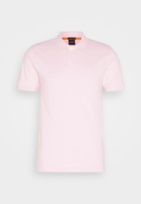 Polo rose pâle en coton, avec une patte de boutonnage à deux boutons, des manches courtes et un petit logo sur la poitrine. Texture lisse.