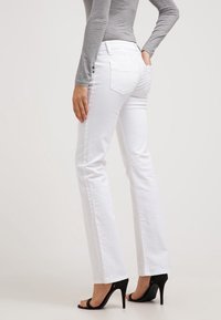 Jeans blancos acampanados de mezclilla con cintura de tiro medio, bolsillos traseros y textura lisa, combinados con sandalias negras de tacón alto.