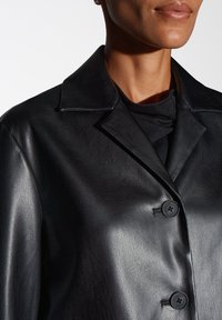 Zwarte leren jas met een gladde textuur, met een kraag, twee knopen en een op maat gemaakte uitstraling. Het materiaal weerkaatst het licht subtiel.