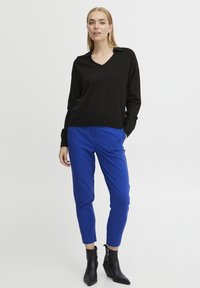 Fekete V nyakú pulóver, laza fit, élénk kék, tapered nadrággal párosítva. A modellen fekete, hegyes orrú és sarkú bokacsizma van.