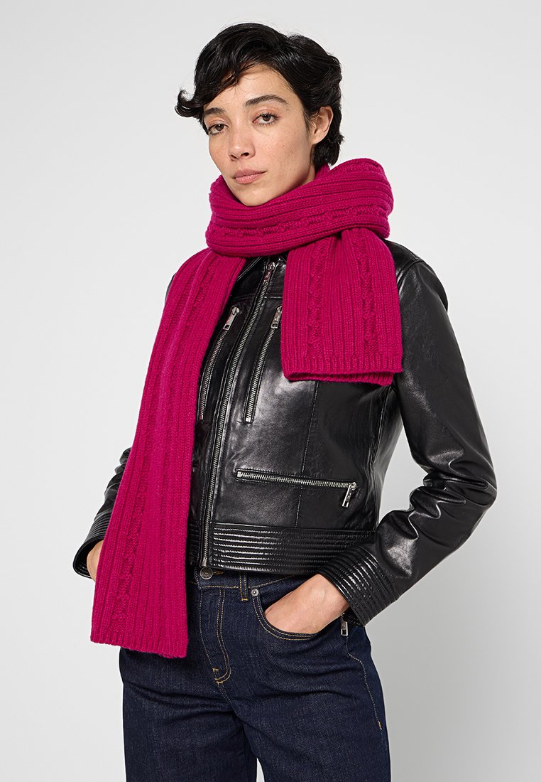 Magenta gestrickter Schal mit strukturiertem Rippenmuster, über einer schwarzen Lederjacke getragen. Der Schal ist um den Hals gewickelt und hängt herunter.