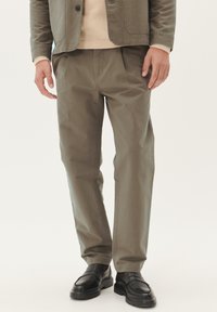 Pantaloni din bumbac khaki cu o croială lejeră, buzunare laterale și plissuri subtile. Purtați cu un pulover ușor și pantofi din piele negri.