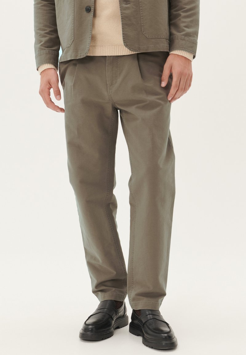 Pantaloni din bumbac khaki cu o croială lejeră, buzunare laterale și plissuri subtile. Purtați cu un pulover ușor și pantofi din piele negri.