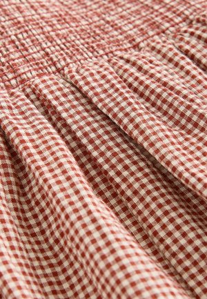 Punase ja valge ginghami kangas kogutud tekstuuri ja volditud detailidega. Materjal näib kerge ja on paigutatud kattuvatesse voltidesse.