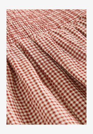 Țesătură gingham roșie și albă cu textură adunată și detalii plisate. Materialul pare ușor și este aranjat în pliuri suprapuse.