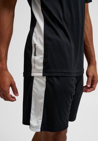 Sort atletisk t-shirt med hvide sidepaneler og logo, parret med sorte shorts med lignende hvide accenter og glat stoftekstur.