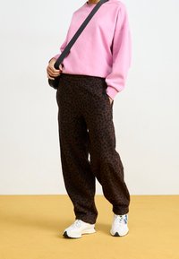Felpa rosa con spalle basse, abbinata a pantaloni leopardati marroni scuri. Il modello indossa sneakers bianche e tiene una borsa a tracolla.