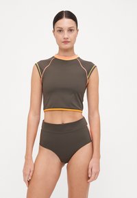 Braunes sportliches Cropped-Top mit orangen Akzenten, kombiniert mit braunen High-Waist-Hosen, die seitliche Einsätze in kontrastierenden Farben haben. Weicher Stoff.