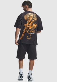 Camiseta negra de gran tamaño con un gráfico de un tigre naranja en la parte posterior. Combinada con pantalones cortos negros y calcetines blancos, y zapatillas negras y blancas.