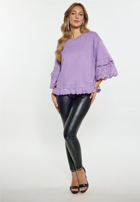 Lavanderen sweater met golvende kanten rand en uitlopende mouwen, gecombineerd met hoogglanzende zwarte leggings en zwarte open schoenen.