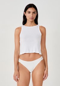 Top corto bianco in tessuto morbido con scollo rotondo, abbinato a slip da bikini bianchi con dettagli in pizzo decorativi sui lati.