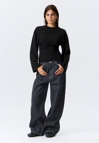 Haut à manches longues noir associé à un jean en denim oversized de couleur foncée. La tenue se compose d'un corps ajusté, de jambes de pantalon amples et d'un tissu texturé.