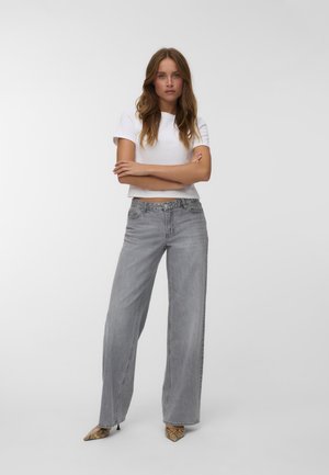 Witte cropped t-shirt, lichtgrijze wijde jeans en puntige slangenhuid hakken. De jeans hebben zijzakken en een klassieke denim uitstraling.