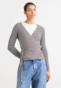 Crno-bijela prugasta slim-fit wrap bluzica s dugim rukavima, V-izrezom i detaljem mašne u struku, u kombinaciji s visokim plavim trapericama.