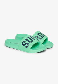 Groene slide-sandalen met een dikke band waarop in vetgedrukte zwarte letters "SUPER" staat. Glad materiaal met een platte zool en afgeronde randen.