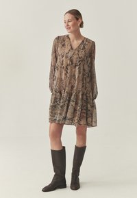 Braunes Kleid mit Schlangenmuster, V-Ausschnitt, langen Ärmeln und einem Rüschensaum. Kombiniert mit kniehohen dunkelbraunen Lederstiefeln. Glatte Textur.