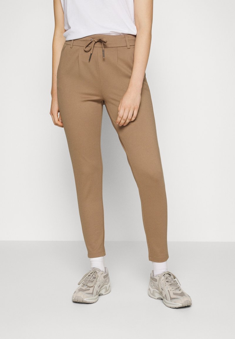 Brown jogger pants in a stretchy fabric, featuring a drawstring waist, tapered legs, and side pockets; paired with light-colored sneakers.